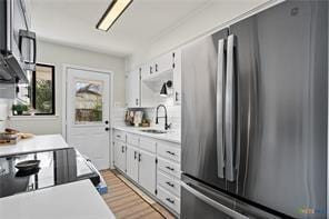 kitchen with white cabinetry, stainless steel fridge, sink, and light hardwood / wood-style flooring