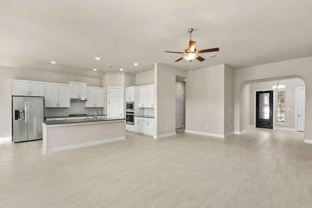 kitchen featuring white cabinetry, appliances with stainless steel finishes, an island with sink, ceiling fan with notable chandelier, and backsplash