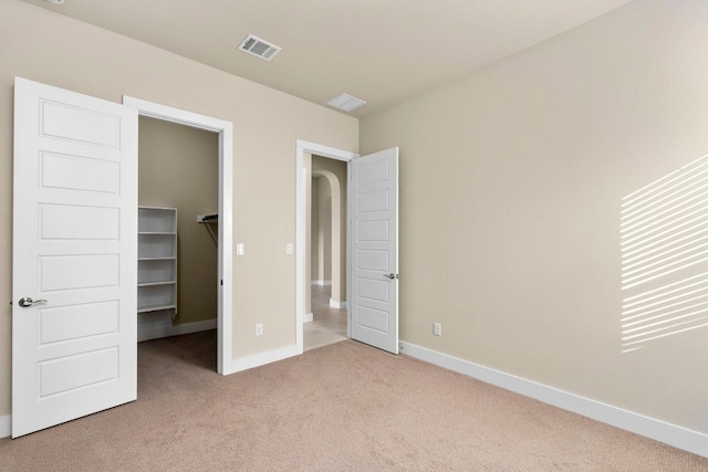 unfurnished bedroom featuring a spacious closet, light colored carpet, and a closet