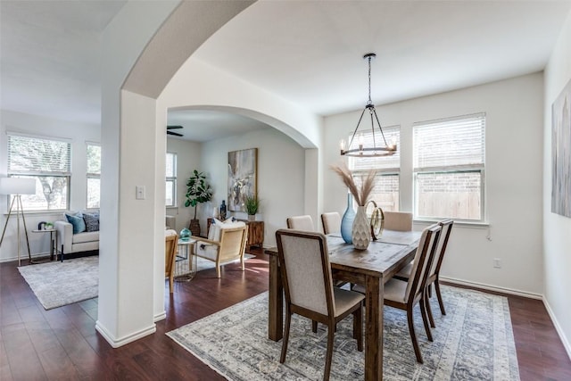 dining space with arched walkways, baseboards, an inviting chandelier, and dark wood finished floors