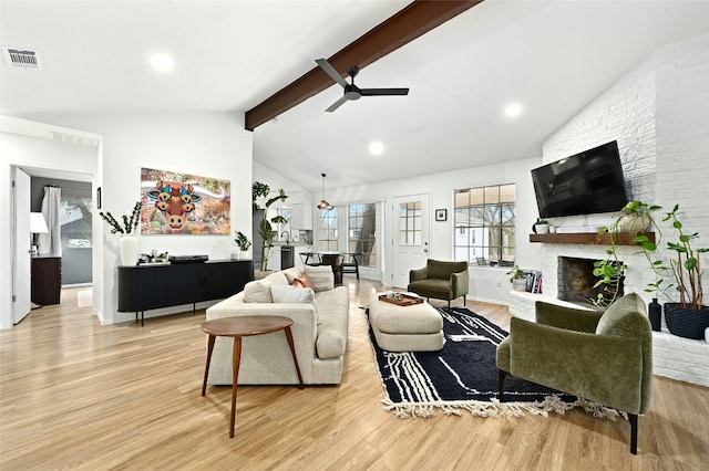 living room featuring high vaulted ceiling, light wood-type flooring, beamed ceiling, ceiling fan, and a fireplace