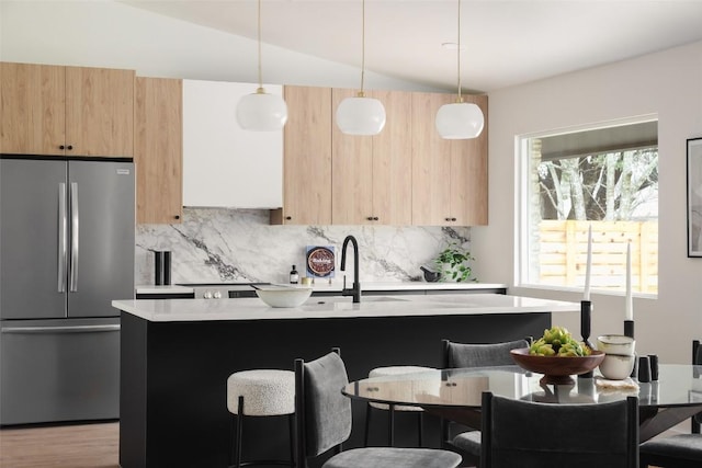 kitchen featuring modern cabinets, light brown cabinetry, freestanding refrigerator, light countertops, and decorative backsplash