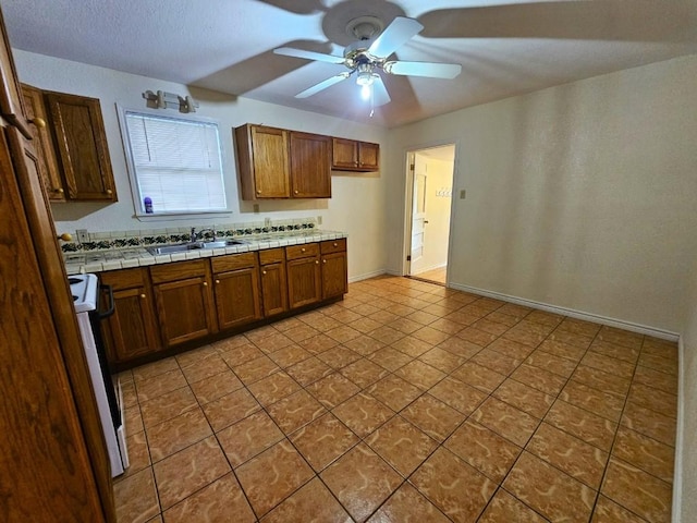 kitchen with sink, range, tile counters, and ceiling fan