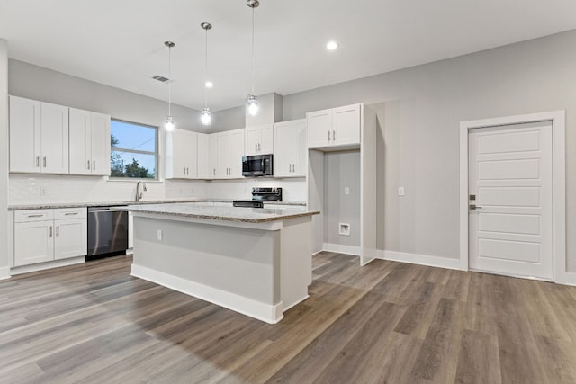 kitchen with stainless steel appliances, light stone countertops, a kitchen island, and white cabinets