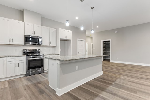 kitchen with appliances with stainless steel finishes, a center island, light stone counters, white cabinets, and decorative light fixtures