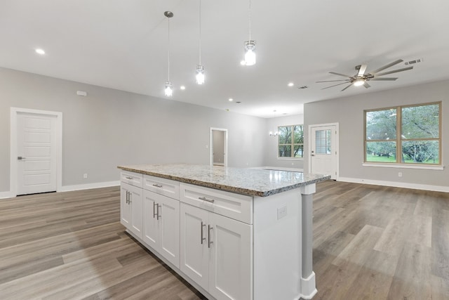 kitchen featuring a kitchen island, white cabinetry, hanging light fixtures, light stone countertops, and light wood-type flooring