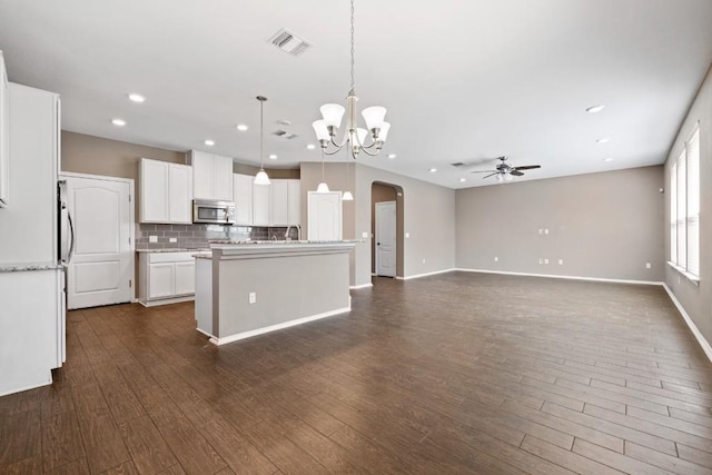 kitchen with dark hardwood / wood-style floors, decorative backsplash, white cabinets, a center island with sink, and decorative light fixtures