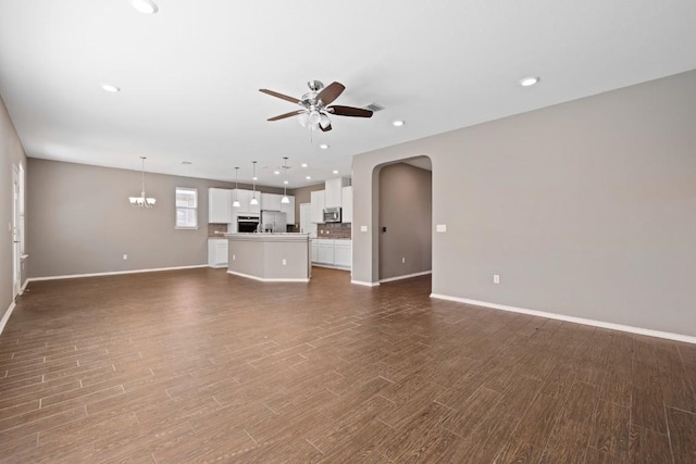 unfurnished living room featuring dark wood-type flooring and ceiling fan with notable chandelier