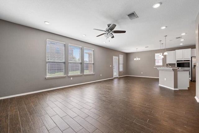 unfurnished living room featuring dark hardwood / wood-style floors, ceiling fan with notable chandelier, and a textured ceiling