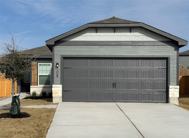 view of front of home with concrete driveway, stone siding, an attached garage, and fence