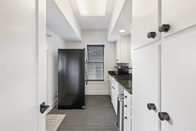 kitchen with sink, black fridge, dark stone countertops, dark tile patterned floors, and white cabinets