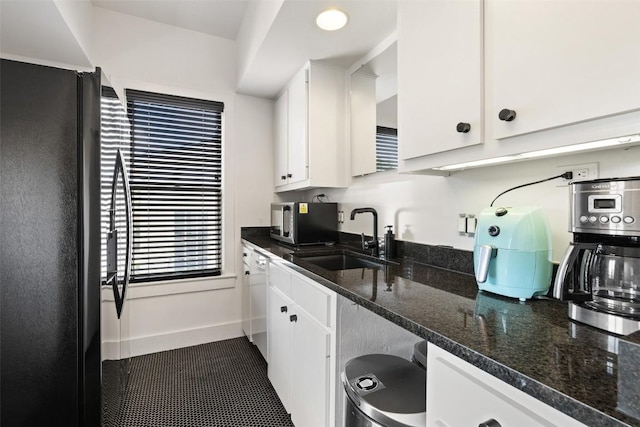 kitchen featuring sink, black fridge, white dishwasher, dark stone counters, and white cabinets