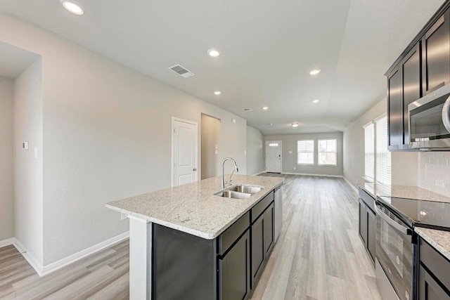 kitchen with light stone counters, appliances with stainless steel finishes, an island with sink, and sink