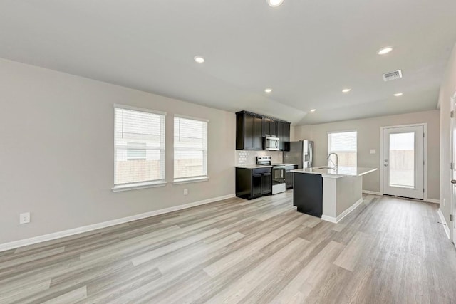 kitchen featuring sink, a center island with sink, light hardwood / wood-style flooring, stainless steel appliances, and backsplash