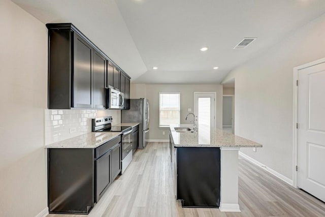 kitchen with tasteful backsplash, an island with sink, sink, stainless steel appliances, and light stone countertops