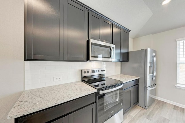 kitchen with tasteful backsplash, light stone countertops, light hardwood / wood-style flooring, and stainless steel appliances