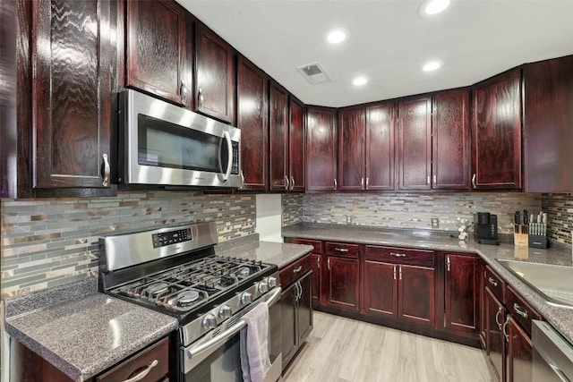 kitchen featuring sink, dark stone countertops, decorative backsplash, stainless steel appliances, and light hardwood / wood-style flooring