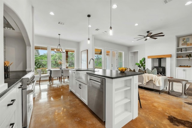 kitchen featuring concrete flooring, appliances with stainless steel finishes, sink, white cabinets, and a kitchen island with sink