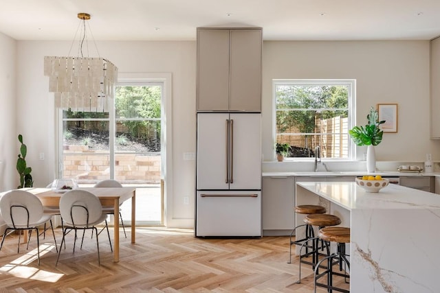 kitchen with sink, hanging light fixtures, white built in fridge, light parquet flooring, and light stone countertops