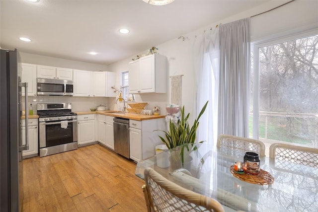 1406 Webberville Rd, Austin, TX 78721 - kitchen with appliances with stainless steel finishes, white cabinetry, light wood-style floors, and recessed lighting