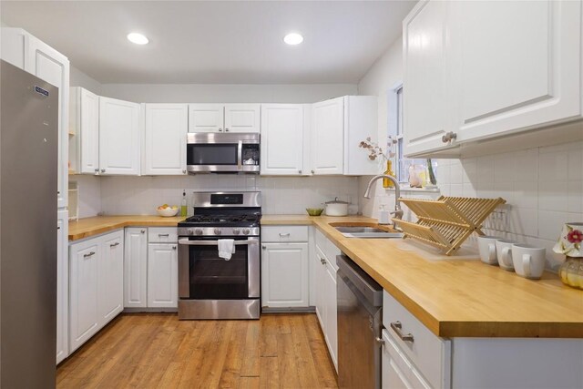 1406 Webberville Rd, Austin, TX 78721 - kitchen with stainless steel appliances, wood counters, light wood finished floors, white cabinetry, and backsplash