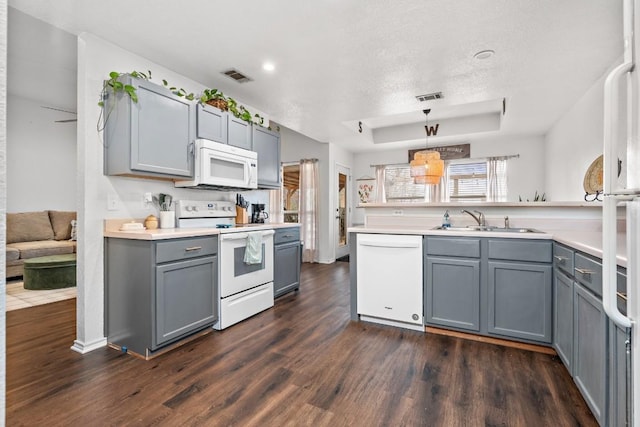 kitchen featuring gray cabinets, sink, hanging light fixtures, a tray ceiling, and white appliances