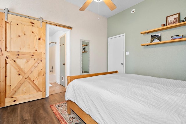 bedroom featuring a barn door, dark hardwood / wood-style floors, connected bathroom, and ceiling fan