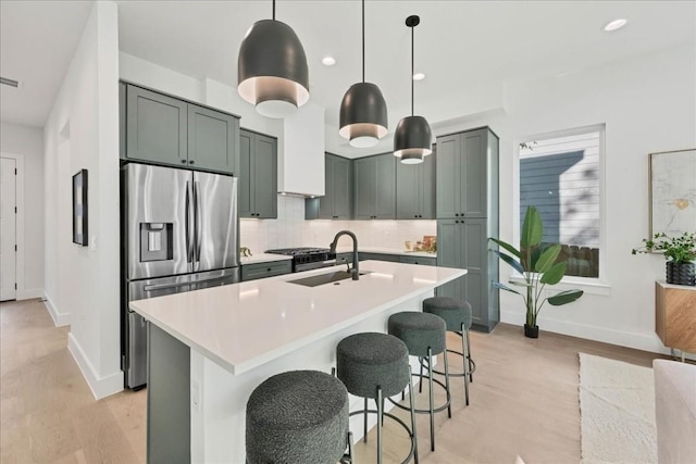 kitchen with stainless steel fridge, hanging light fixtures, tasteful backsplash, an island with sink, and a kitchen bar