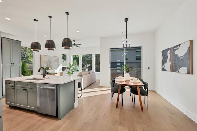 kitchen with sink, a kitchen island with sink, hanging light fixtures, stainless steel dishwasher, and light wood-type flooring