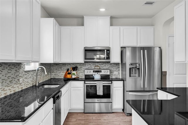 kitchen with sink, dark stone counters, stainless steel appliances, white cabinets, and tasteful backsplash