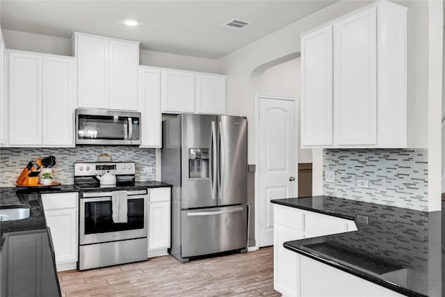 kitchen with dark stone counters, appliances with stainless steel finishes, white cabinets, and light wood-type flooring