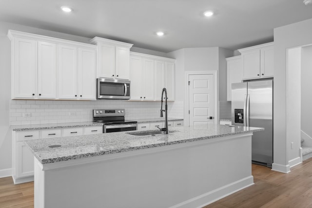 kitchen with appliances with stainless steel finishes, sink, light hardwood / wood-style flooring, white cabinetry, and an island with sink