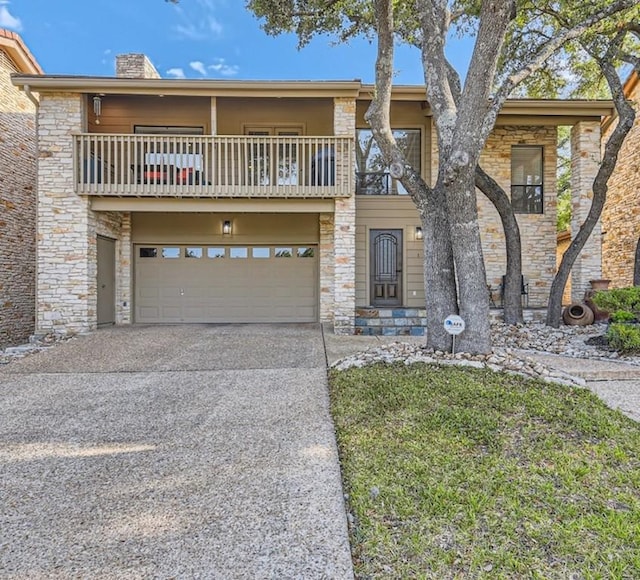 view of front of property with driveway, a balcony, stone siding, a chimney, and an attached garage