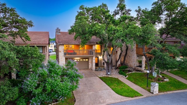 view of front of home with an attached garage, stone siding, concrete driveway, a chimney, and a front yard