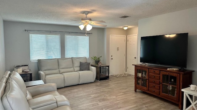 living room with light wood-type flooring, ceiling fan, and a textured ceiling