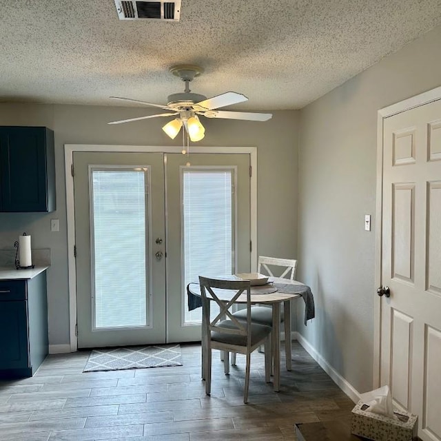 dining space featuring ceiling fan, light wood-type flooring, french doors, and a textured ceiling