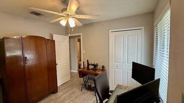 home office with light wood-type flooring, ceiling fan, and a textured ceiling