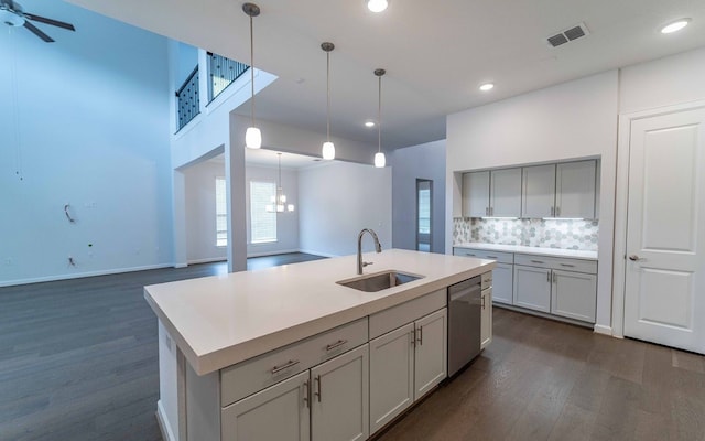 kitchen with dark wood-type flooring, stainless steel dishwasher, pendant lighting, sink, and a kitchen island with sink