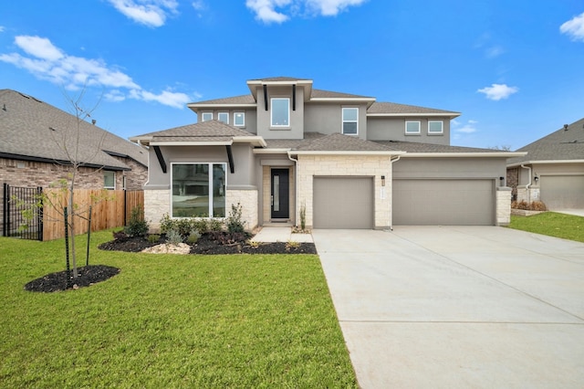prairie-style house featuring driveway, a front yard, fence, an attached garage, and stucco siding