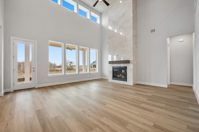 unfurnished living room with visible vents, ceiling fan, a high ceiling, a high end fireplace, and light wood finished floors