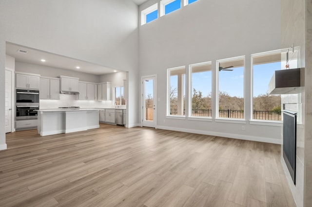 unfurnished living room with baseboards, a glass covered fireplace, light wood-style floors, a high ceiling, and recessed lighting