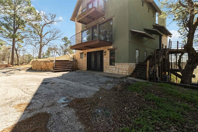 exterior space featuring stairway, stone siding, a balcony, and stucco siding