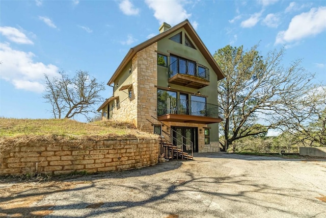 view of front of house with stone siding, a balcony, and a chimney