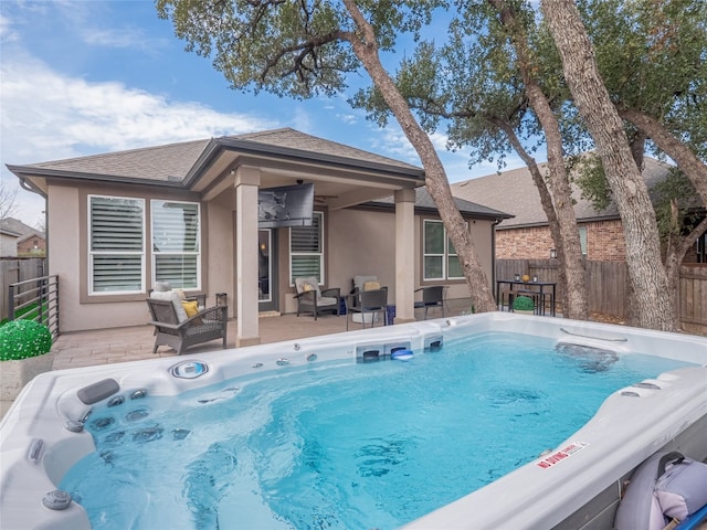 rear view of house with stucco siding, a hot tub, and fence