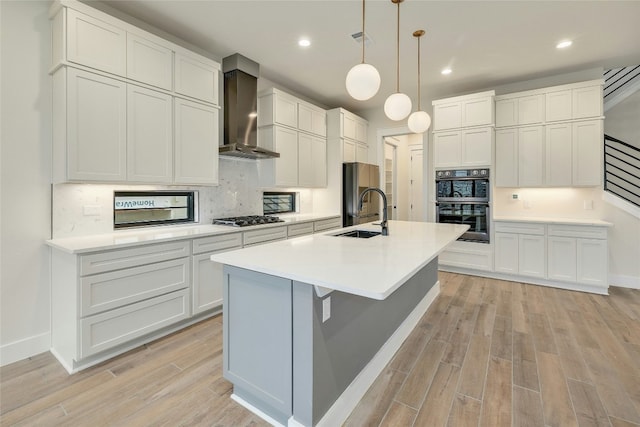 kitchen featuring a center island with sink, stainless steel appliances, decorative light fixtures, sink, and wall chimney exhaust hood