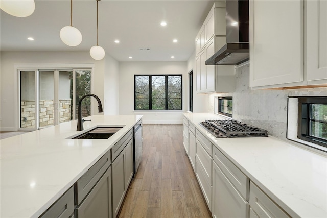 kitchen featuring stainless steel appliances, decorative light fixtures, light stone countertops, sink, and wall chimney exhaust hood