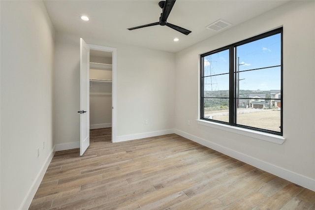 unfurnished bedroom featuring ceiling fan, light hardwood / wood-style flooring, a walk in closet, and a closet