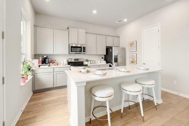 kitchen featuring appliances with stainless steel finishes, a kitchen island with sink, a breakfast bar, and light hardwood / wood-style floors