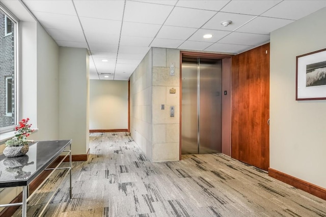 hall with light wood-type flooring, elevator, and a drop ceiling