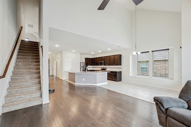 unfurnished living room featuring recessed lighting, ceiling fan with notable chandelier, a towering ceiling, light wood-style floors, and stairs